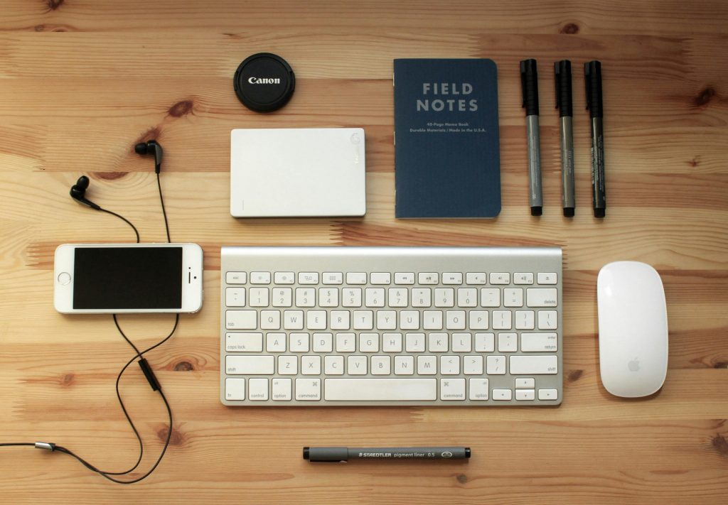 Top view of a modern desk setup featuring electronics, stationery, and gadgets on a wooden surface.